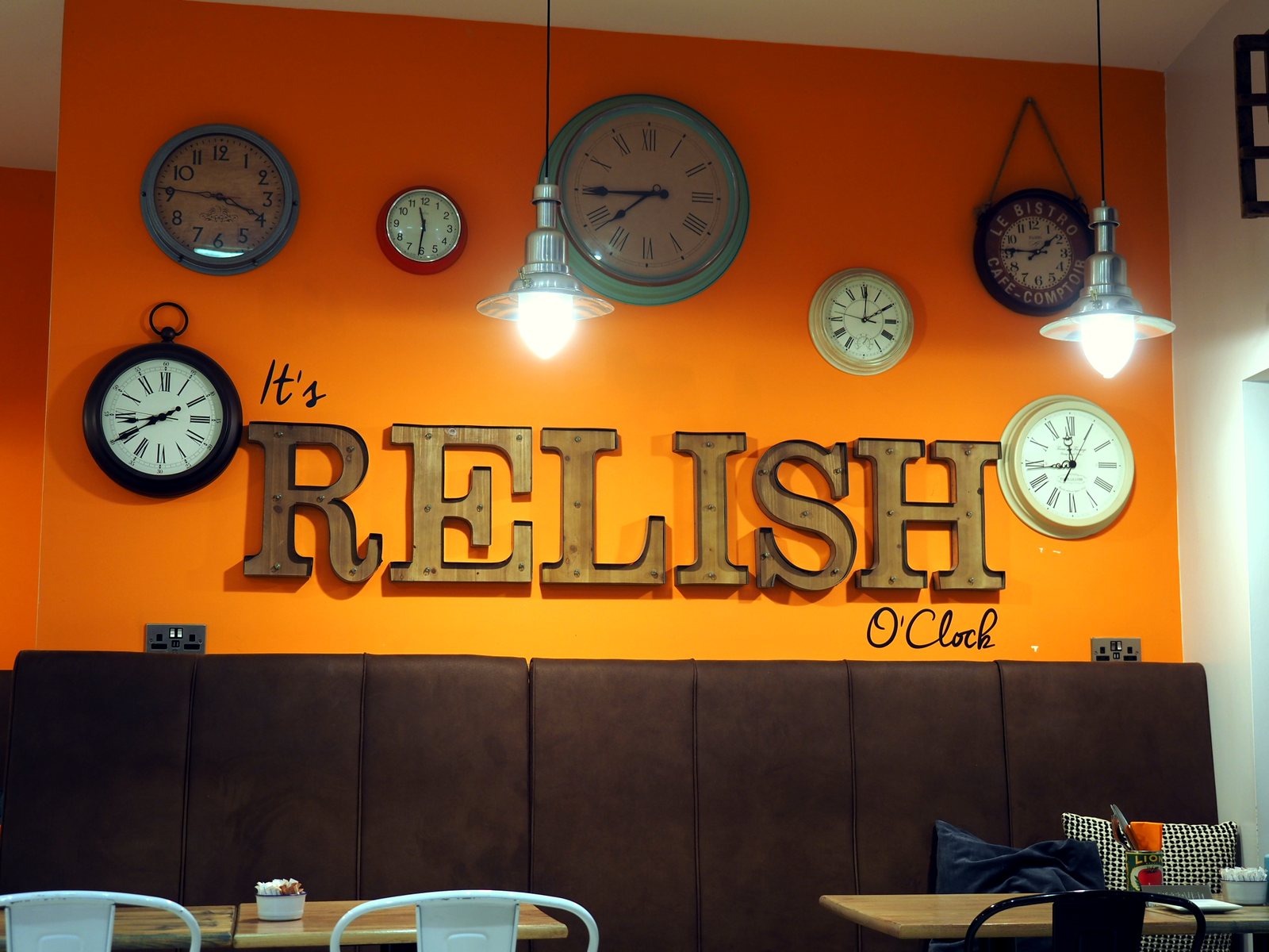 The café's orange wall reading It's Relish O'Clock, surrounded by clocks